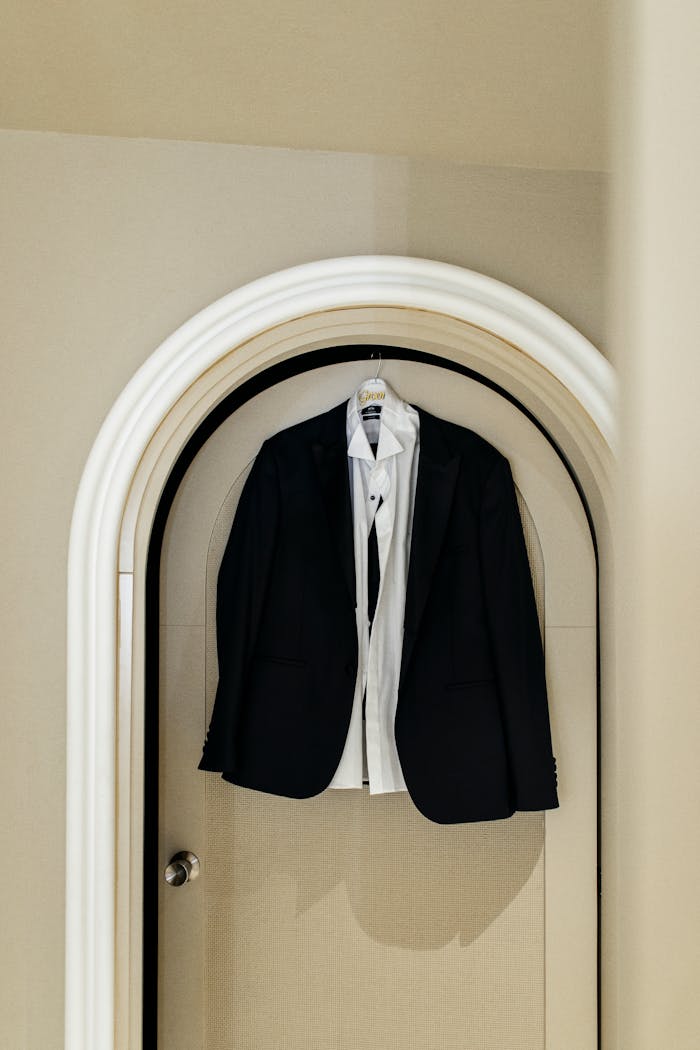 services-03 Classic black suit and white shirt hanging on an arched door, showcasing elegance and sophistication.