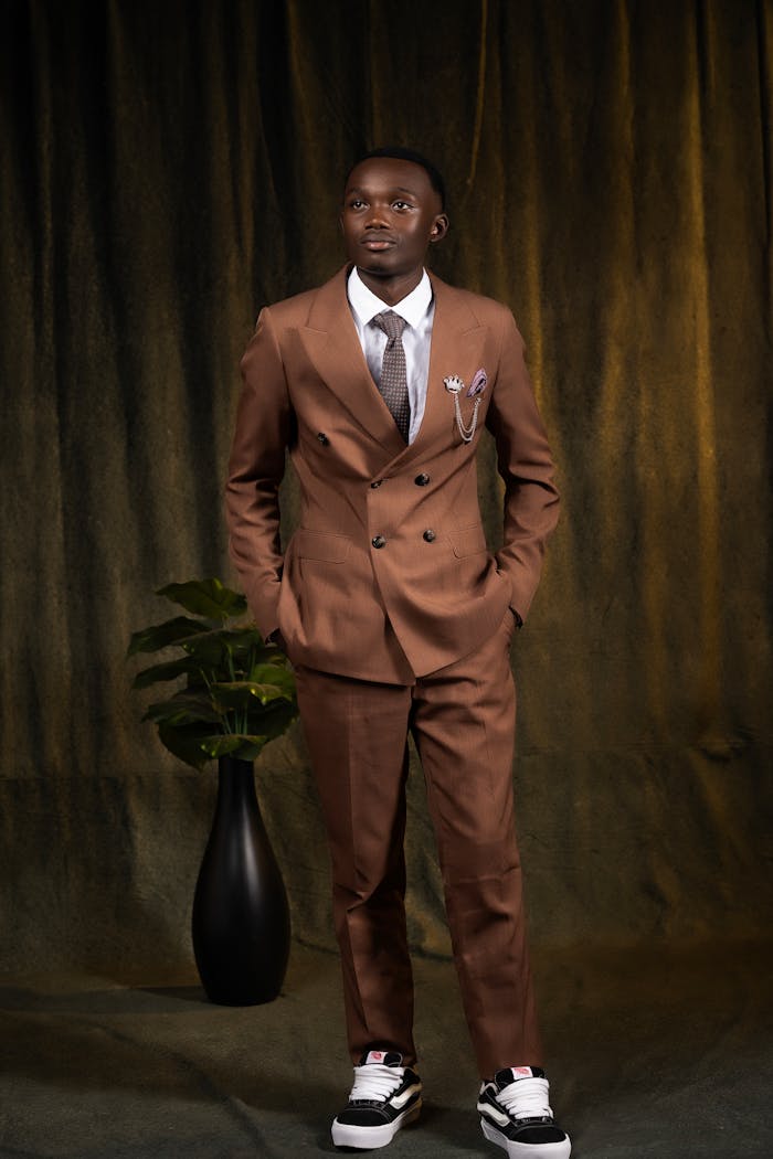 services-04 Man in brown suit and sneakers with plant indoors, warm lighting.
